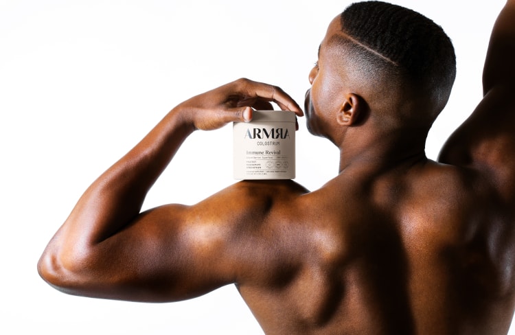 Male model from the back showing back and arm muscles flexed holding ARMRA Immune Revival product on shoulder with white background