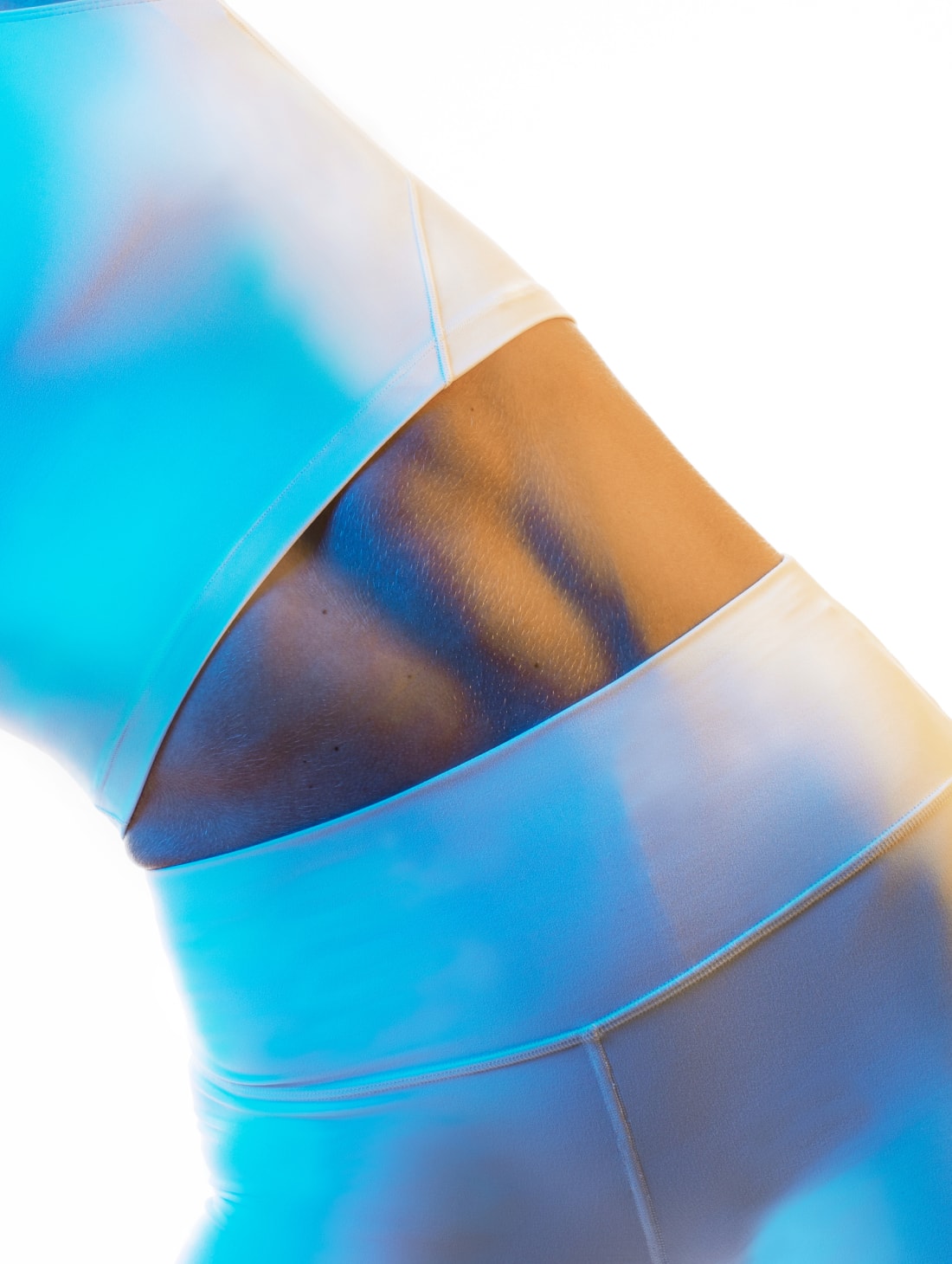The torso of a woman with white leggings and white crop top with abdominal muscles and a bright blue tint to the image with a white background