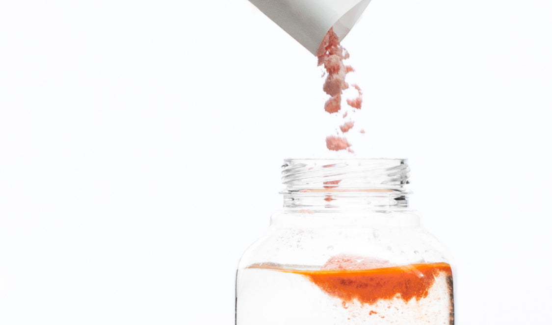 White background with a clear bottle and ARMRA immune revival blood orange product being poured in