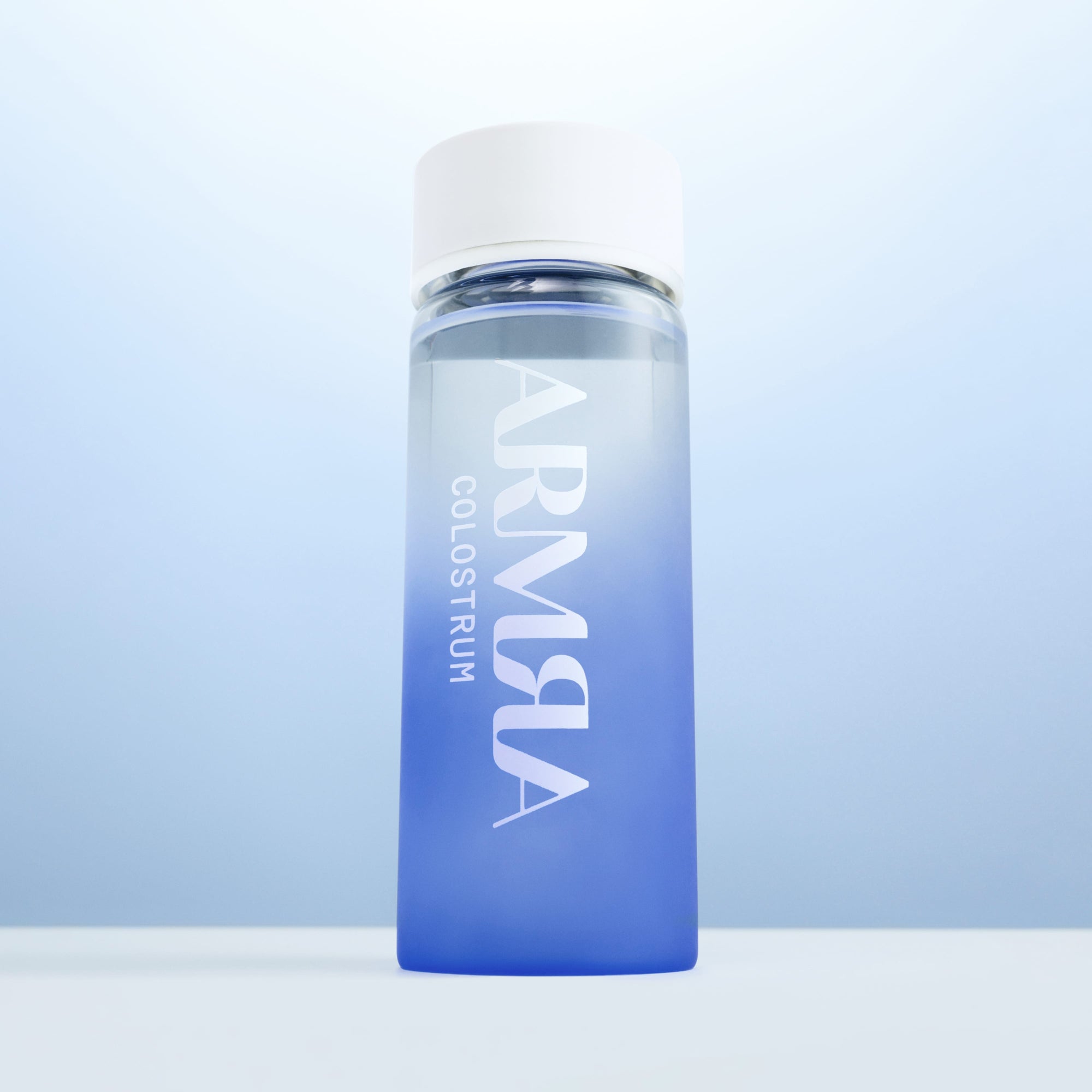 Cream Lid on a glass Water Bottle with blue gradient and “ARMRA Colostrum“ Logo
