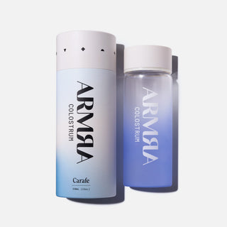 Cylindrical packaging for Water Bottle with “ARMRA Colostrum “logo laying next to a glass Water Bottle with a blue gradient with “ARMRA Colostrum “logo