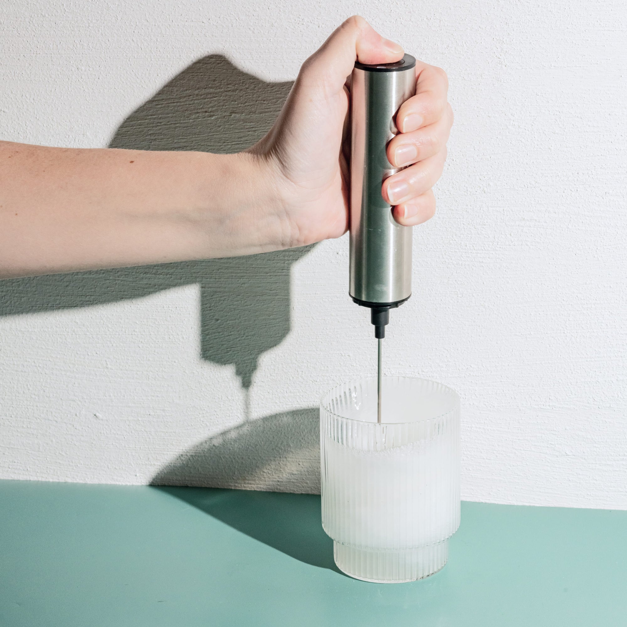 A Person using a Stainless Steel Whirl stirring Colostrum in a glass on a green table top