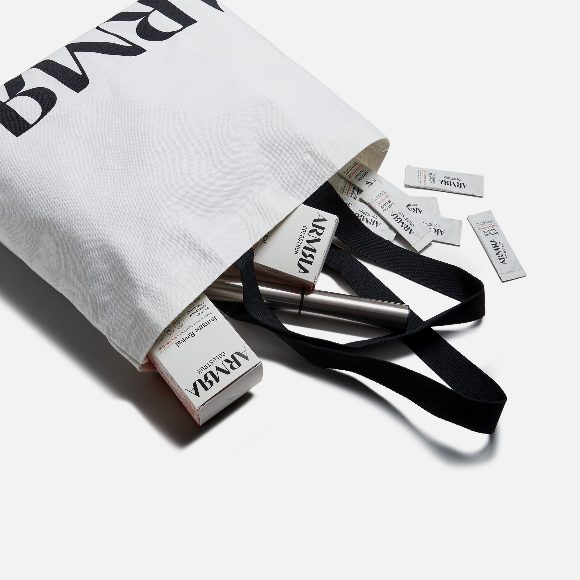 White tote with black handles laying down with product boxes, product pouches and stainless steel spilling out